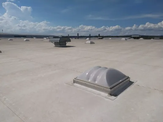 Techo industrial plano con membrana blanca y varios domos de policarbonato a lo lejos para maximizar la luz natural interior.