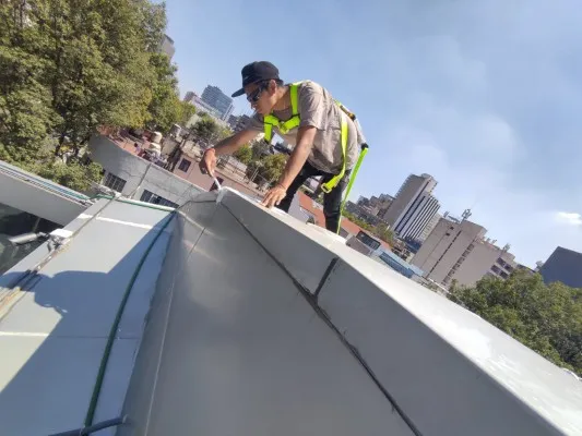 Trabajador en azotea con equipo de seguridad realizando limpieza y mantenimiento. Aprende bien qué es un canalón y cómo cuidarlo.